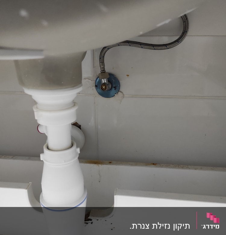 צינור ניקוז לבן מתחת לכיור עם חיבור מתכת